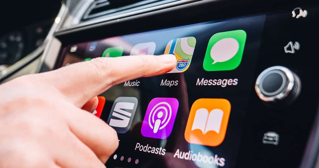 Car panel showing CarPlay with a person touching the Maps icon